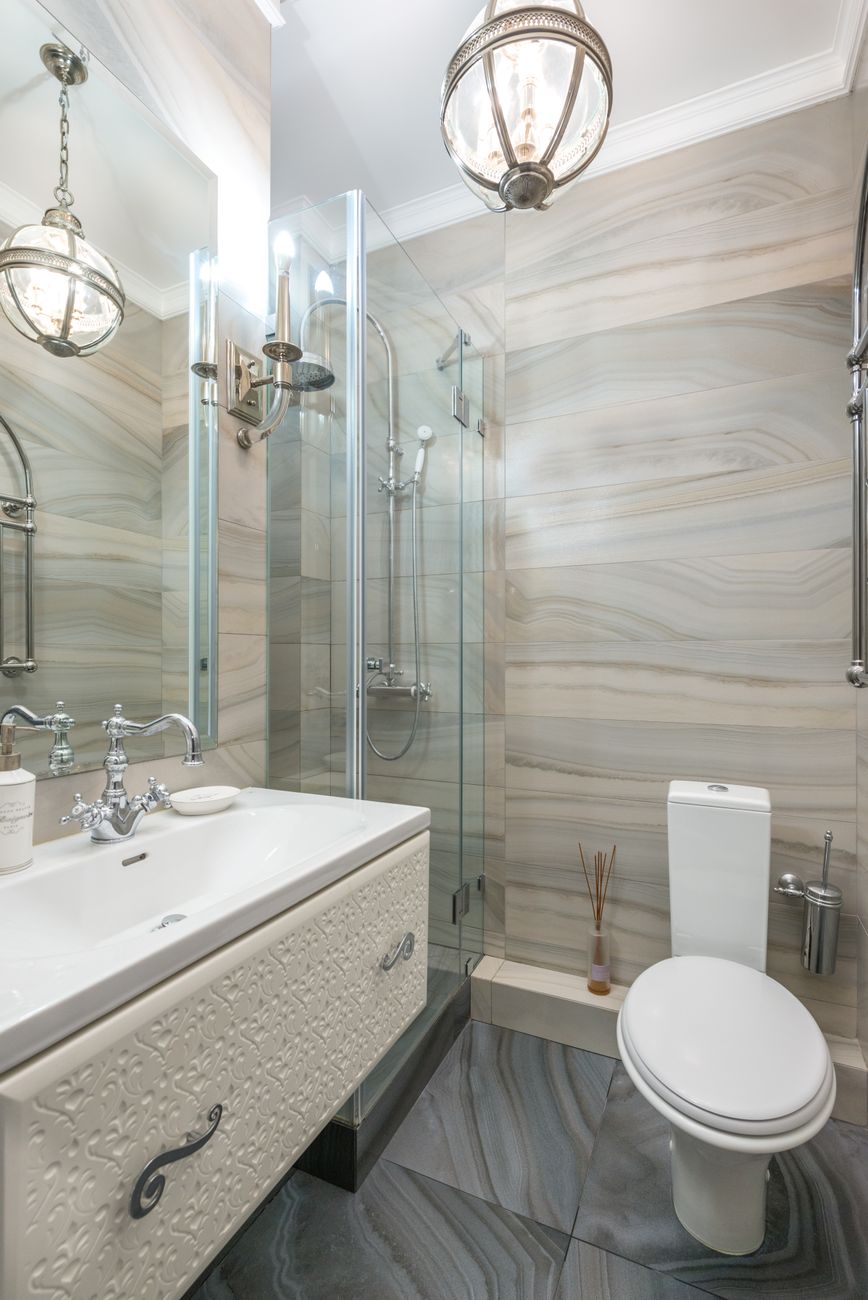 A narrow separate WC with a closed toilet lid, a small basin and a wall lamp