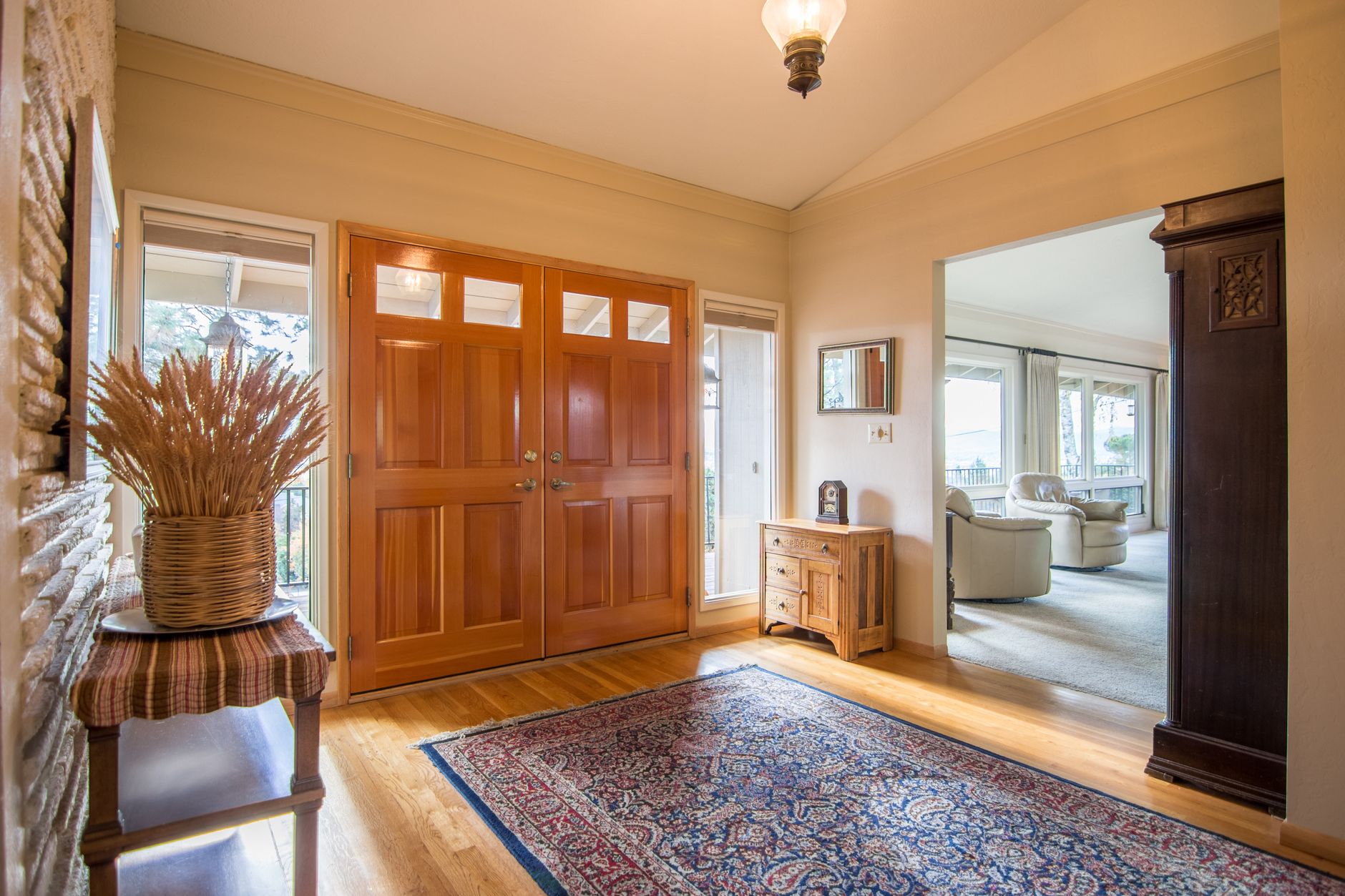 An entrance hall with a rug in front of the door, a console table, a small cabinet and an opening into the living room