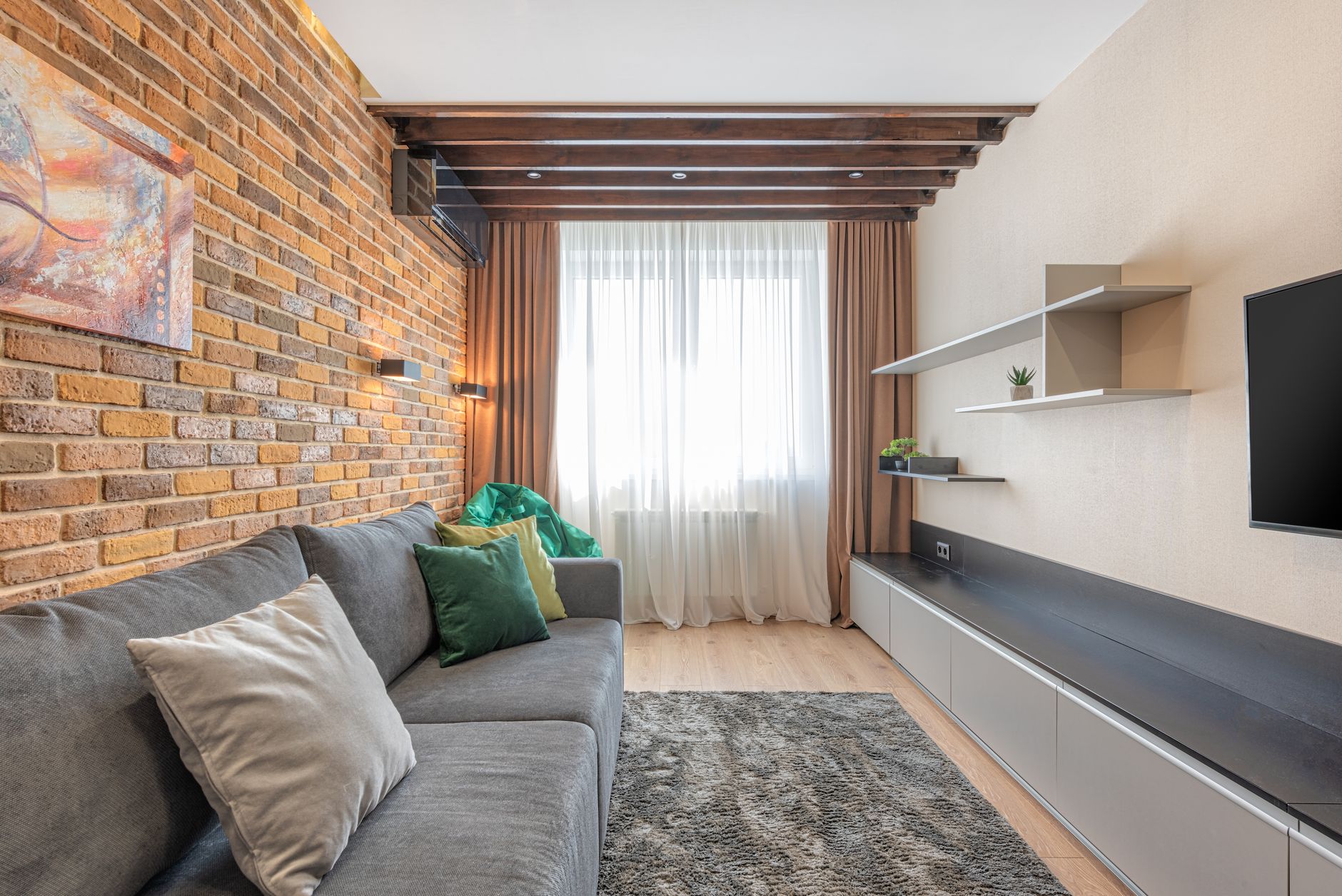A sofa pushed back against a solid brick wall, facing a long low media unit with a wall mounted television across a rug