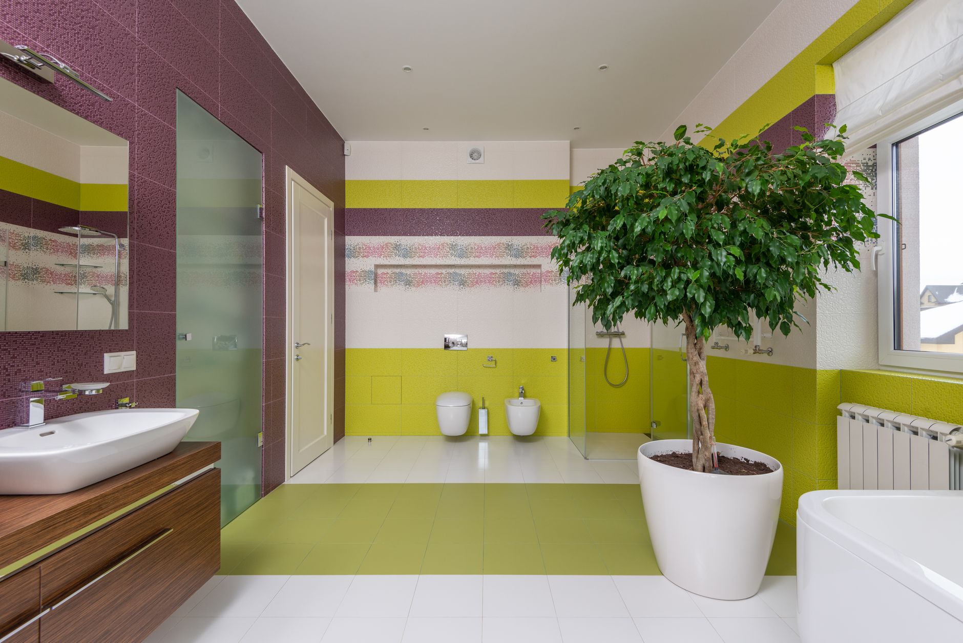 A bright bathroom with a window, pale tiles and a plant on the shelf